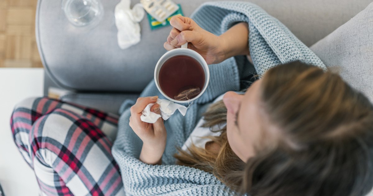 Person wrapped in a blanket on the couch holding a mug of herbal tea during cold and flu season